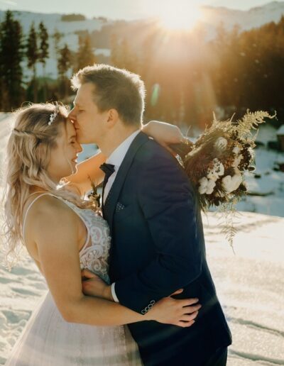 Brautpaar bei ihrer Winterhochzeit in den Bergen beim Shooting im Sonnenuntergang mit Brautstrauß